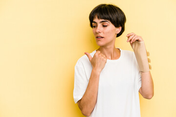 Young caucasian woman hand sling isolated on yellow background points with thumb finger away, laughing and carefree.