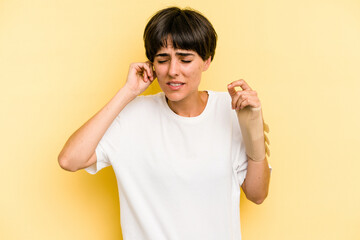 Young caucasian woman hand sling isolated on yellow background covering ears with hands.