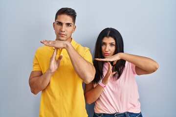 Young couple standing over isolated background doing time out gesture with hands, frustrated and...