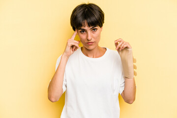 Young caucasian woman hand sling isolated on yellow background pointing temple with finger,...