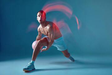 Basketball player athletic modern male dribbling ball with naked torso in neon light. Long exposure, motion blur. Sports