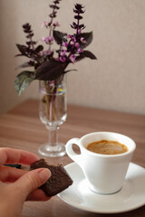 espresso in small white cup, hand taking bitten piece of chocolate from saucer
