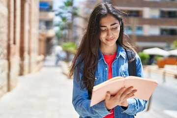 Young hispanic girl student writing on notebook at street