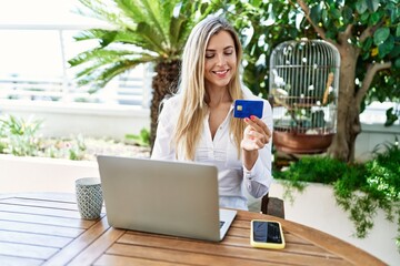 Young blonde woman buying using laptop and credit card at the terrace.