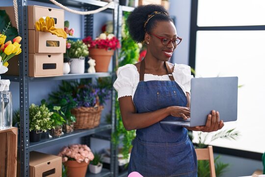African american woman florist smiling confident using laptop at florist store