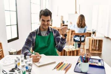 Young artist man at art studio very happy and excited doing winner gesture with arms raised, smiling and screaming for success. celebration concept.