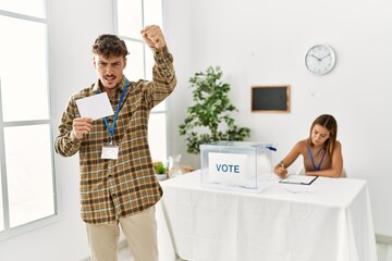 Young handsome man voting putting envelop in ballot box annoyed and frustrated shouting with anger,...