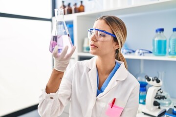 Young hispanic woman scientist measuring liquid at laboratory