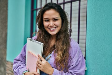 Fototapeta premium Young hispanic student woman smiling happy holding books at the city.