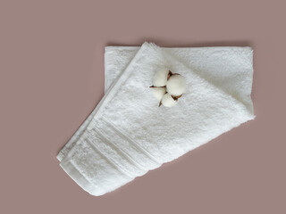 Folded white cotton towel with a flower of cotton on the beige background.