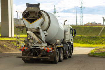 Grey mixer truck on city road is transporting cement to building site - obrazy, fototapety, plakaty