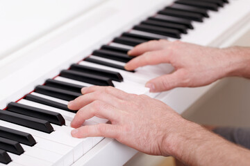 Fototapeta premium Young man playing on white modern piano, home learning, music education, composing