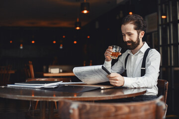 Bearded man sits at a table and drinks alcohol.