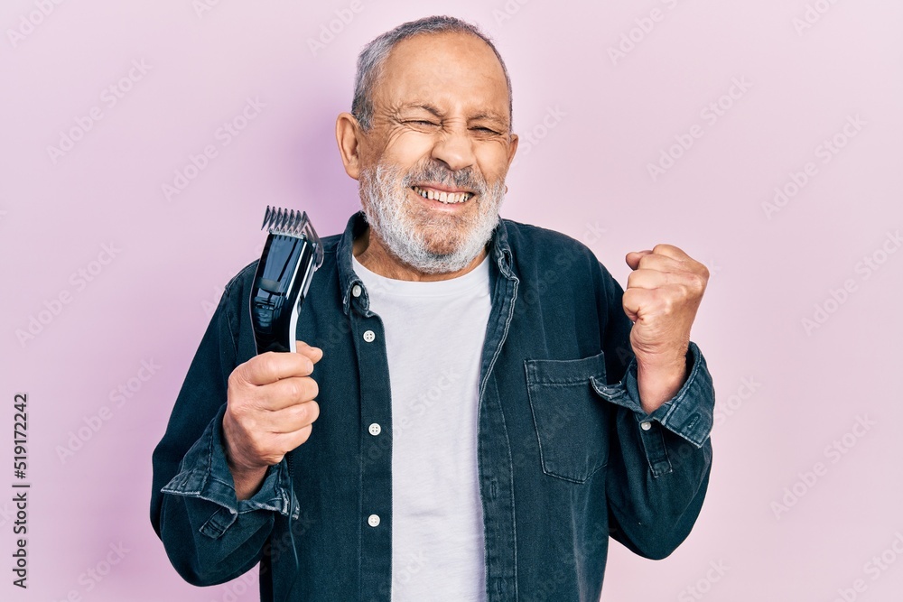 Poster handsome senior man with beard holding electric razor machine screaming proud, celebrating victory a