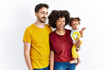 Interracial young family of black mother and hispanic father with daughter winking looking at the camera with sexy expression, cheerful and happy face.