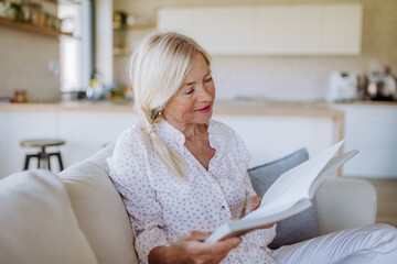Senior woman sitting on sofa and reading book at home