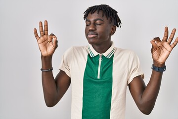 African man with dreadlocks standing over isolated background relaxed and smiling with eyes closed doing meditation gesture with fingers. yoga concept.