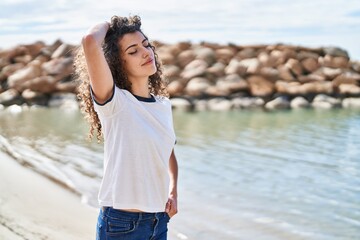 Young hispanic woman smiling confident relaxed with hand on head at seaside