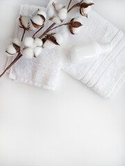 White towels with cotton flower branch and white plastic bottle for cosmetics on the white background.