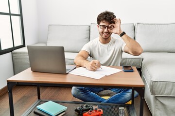 Hispanic man doing papers at home doing ok gesture with hand smiling, eye looking through fingers with happy face.