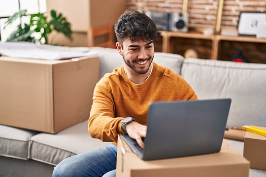 Young hispanic man smiling confident using laptop at new home