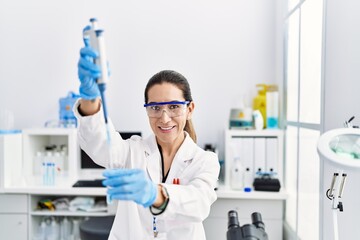 Fototapeta premium Young hispanic woman wearing scientist uniform using pipette at laboratory