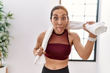 Young hispanic woman wearing sportswear and towel at sport center sticking tongue out happy with funny expression.