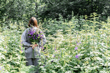 portrait of a girl in a gray satin suit among the tall grass. a model with long straight hair holds a bouquet of field herbs in the forest. the concept of femininity.