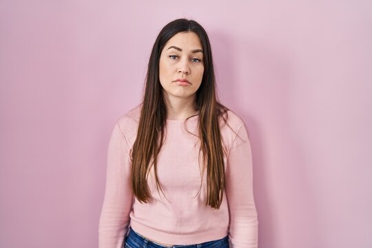 Young brunette woman standing over pink background looking sleepy and tired, exhausted for fatigue and hangover, lazy eyes in the morning.
