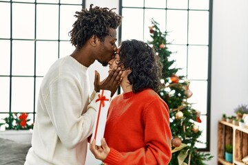 Young interracial couple smiling happy and hugging holding christmas gift at home.