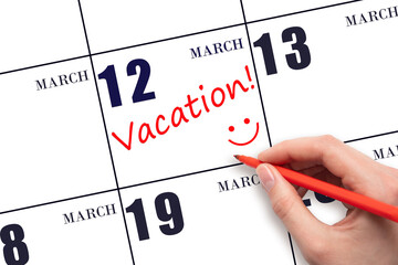 12th day of March. A hand writing a VACATION text and drawing a smiling face on a calendar date 12...