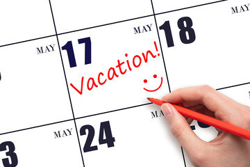 17th day of May. A hand writing a VACATION text and drawing a smiling face on a calendar date 17...
