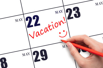 22nd day of May. A hand writing a VACATION text and drawing a smiling face on a calendar date 22...