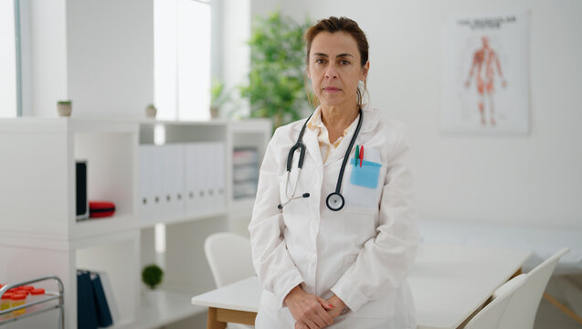 Middle age hispanic woman wearing doctor uniform standing with relaxed expression at clinic