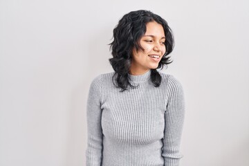 Hispanic woman with dark hair standing over isolated background looking away to side with smile on face, natural expression. laughing confident.