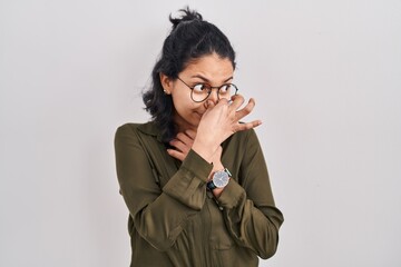 Hispanic woman with dark hair standing over isolated background smelling something stinky and...