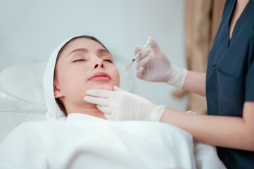 Fototapeta premium Girl beautician makes injections on the lips and face of a beautiful woman in a cosmetic wedge.