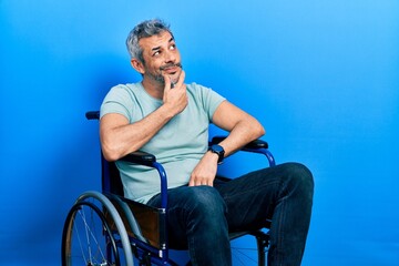 Handsome middle age man with grey hair sitting on wheelchair thinking worried about a question,...