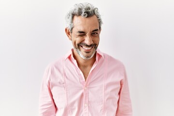 Middle age hispanic man standing over isolated background winking looking at the camera with sexy...