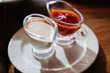 saucepans with white and red sauces in a white plate on a wooden table.