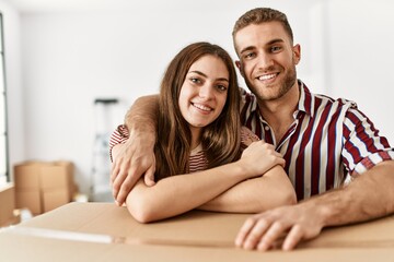 Young caucasian couple smiling happy leaning on cardboard box at new home.