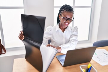 African american woman business worker opening binder using laptop at office