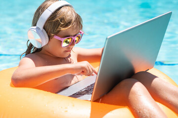 Child working on laptop in summer pool. Little freelancer using computer, remote working in poolside.