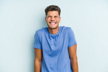 Fototapeta na wymiar Young caucasian man isolated on blue background laughs and closes eyes, feels relaxed and happy.