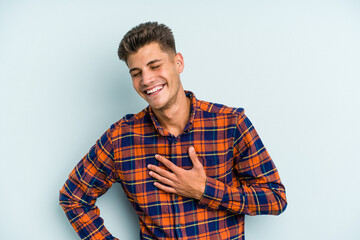 Young caucasian man isolated on blue background laughing keeping hands on heart, concept of happiness.