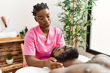 Young physiotherapist woman giving head massage to african american man at the clinic.