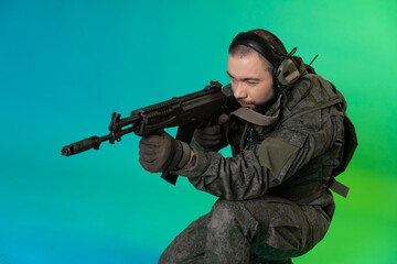 Fototapeta premium soldier in the studio on a green background with colored light. a man in military uniform with a gun, rifle or machine gun. military. airball player