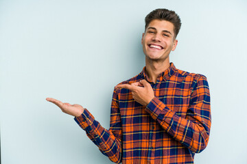 Young caucasian man isolated on blue background excited holding a copy space on palm.