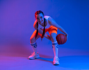 girl with a basketball in orange shorts, a t-shirt. an athlete in golfs and sneakers on a blue background plays the ball. Physical education teacher. basketball player. in move. blur. the game