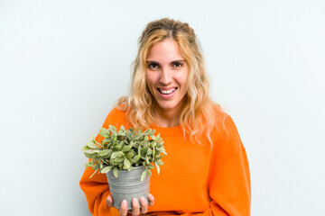 Young caucasian woman holding a plant isolated on blue background laughing and having fun.